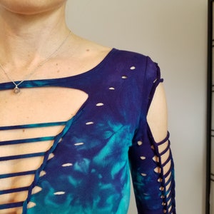 Pu&ograve; includere: Una camicia a maniche lunghe in tie-dye blu e turchese con un design a taglio e dettagli in pizzo sul davanti e sulle maniche.
