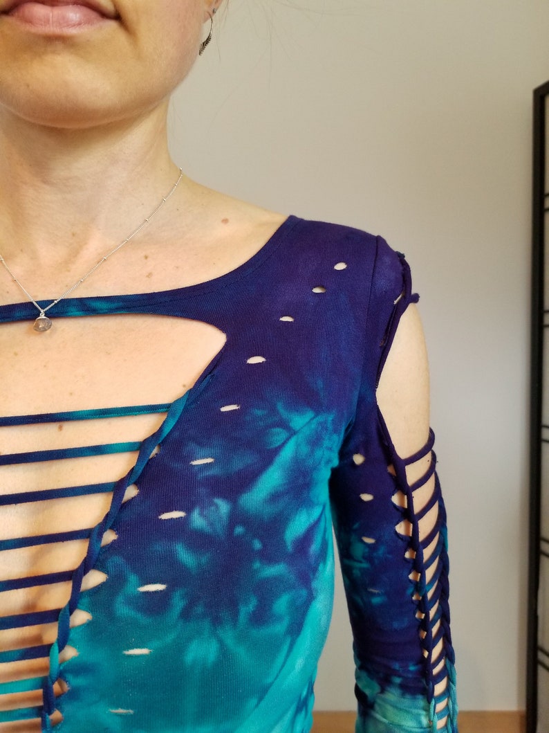 Pu&ograve; includere: Una camicia a maniche lunghe in tie-dye blu e turchese con un design a taglio e dettagli in pizzo sul davanti e sulle maniche.