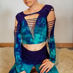 Pu&ograve; includere: Un top corto a maniche lunghe con un motivo tie-dye in tonalit&agrave; blu e verdi. Il top ha una profonda scollatura a V con un design a traliccio e dettagli ritagliati sulle maniche.