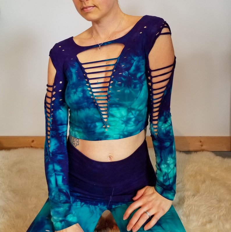 Pu&ograve; includere: Un top corto a maniche lunghe con un motivo tie-dye in tonalit&agrave; blu e verdi. Il top ha una profonda scollatura a V con un design a traliccio e dettagli ritagliati sulle maniche.