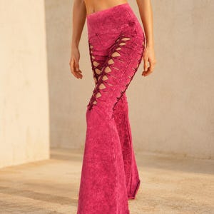 Puede incluir: Pantalones acampanados de talle alto en un acabado magenta vibrante con efecto lavado al ácido. Estos pantalones presentan un diseño distintivo de cordones a lo largo de los laterales exteriores de cada pierna, con tiras cruzadas de tela.