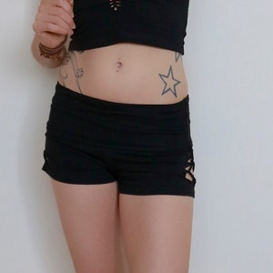 May include: Black shorts with a criss-cross detail on the side. The shorts are made of a soft, stretchy fabric and have a low rise.