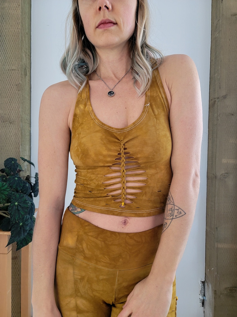 May include: A mustard yellow halter top with a braided detail and cutouts. The top is made of a soft, flowy fabric and has a relaxed fit.