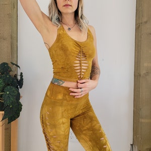 May include: A mustard yellow crop top with a lace-up detail in the front and matching leggings. The top and leggings are made of a soft, stretchy fabric.