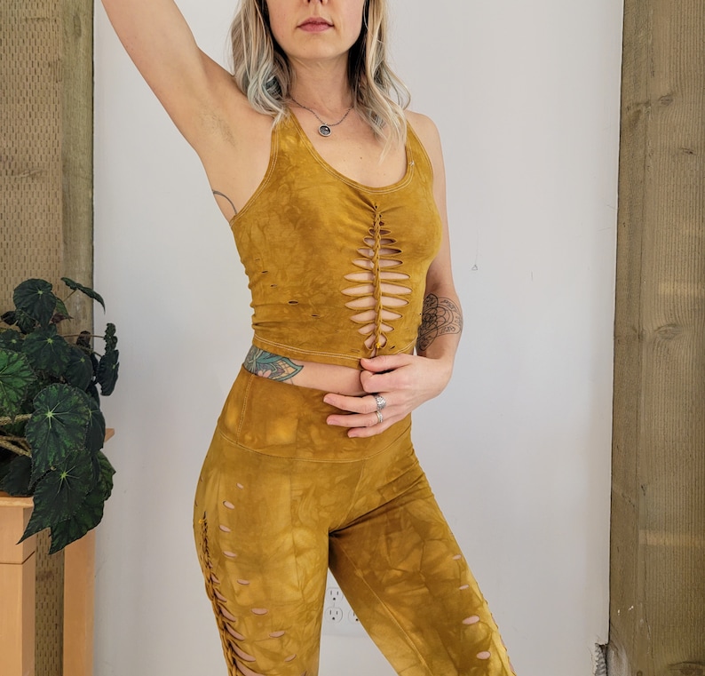 May include: A mustard yellow crop top with a lace-up detail in the front and matching leggings. The top and leggings are made of a soft, stretchy fabric.