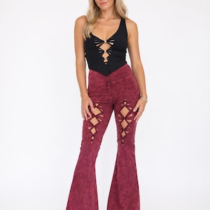 May include: A black tank top with a plunging neckline and cut-out details is paired with burgundy flare pants. The pants feature cut-out designs on the thighs. The outfit has a bohemian style.