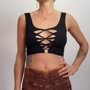 May include: Black crop top with a criss-cross lace-up design in the front. The top has a scoop neckline and a ring detail at the center.