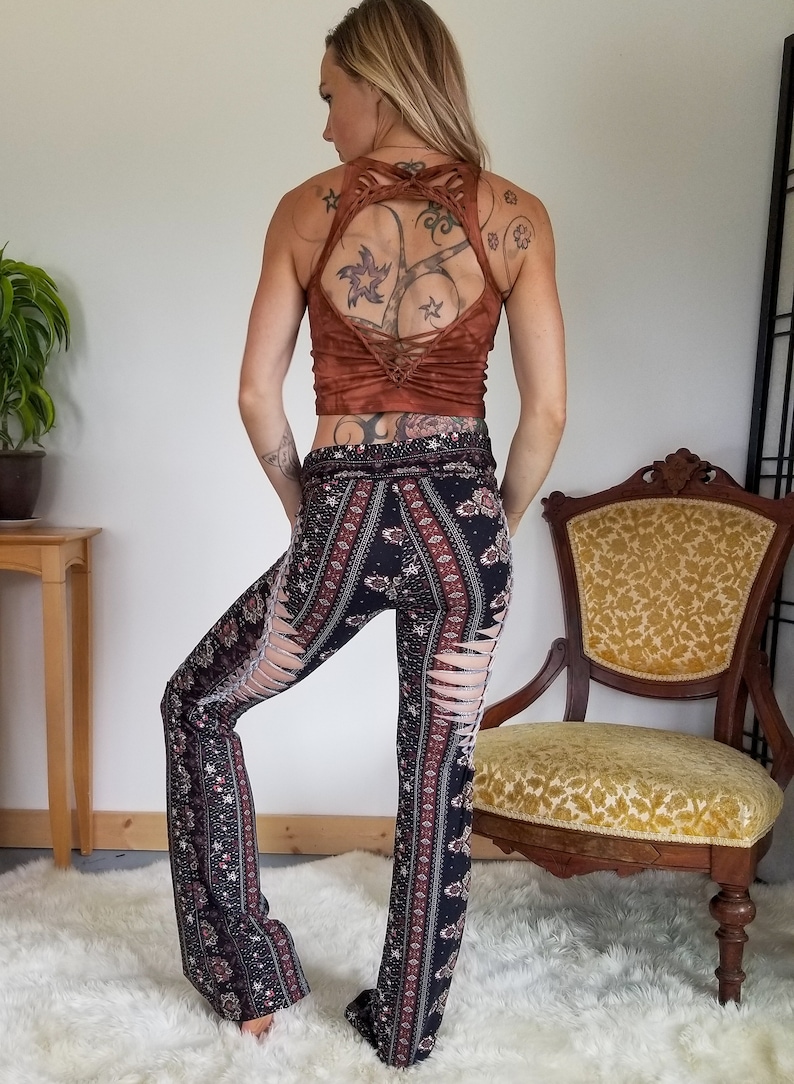 Pode incluir: Cal&ccedil;as de boca de sino com padr&atilde;o preto e vermelho e fendas nas laterais. As cal&ccedil;as s&atilde;o usadas por uma pessoa com um top curto marrom e tatuagens.
