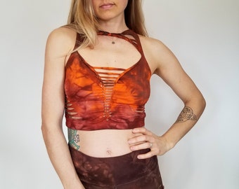 May include: A tie-dye crop top with a criss-cross design in shades of orange and brown. The top has a racerback style and is made of a soft, stretchy fabric.