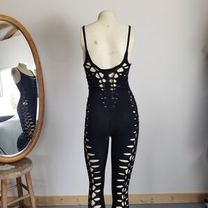 May include: Black jumpsuit with cut-outs on the legs and back. The jumpsuit is made from a stretchy fabric and has a fitted silhouette.