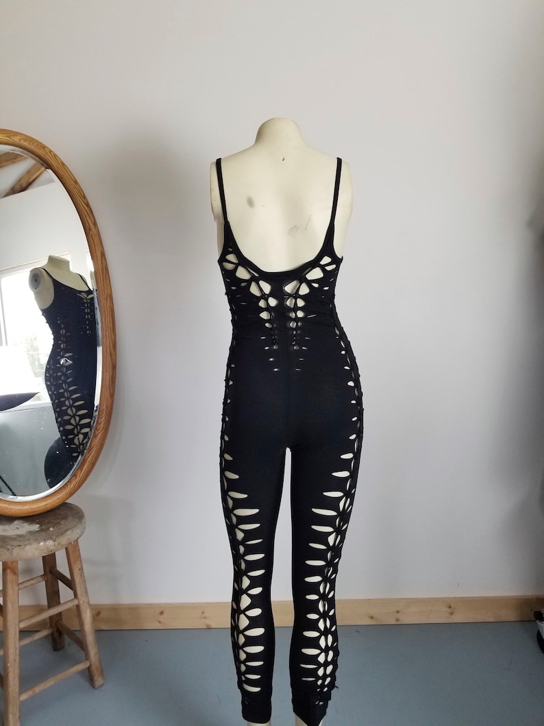 May include: Black jumpsuit with cut-outs on the legs and back. The jumpsuit is made from a stretchy fabric and has a fitted silhouette.