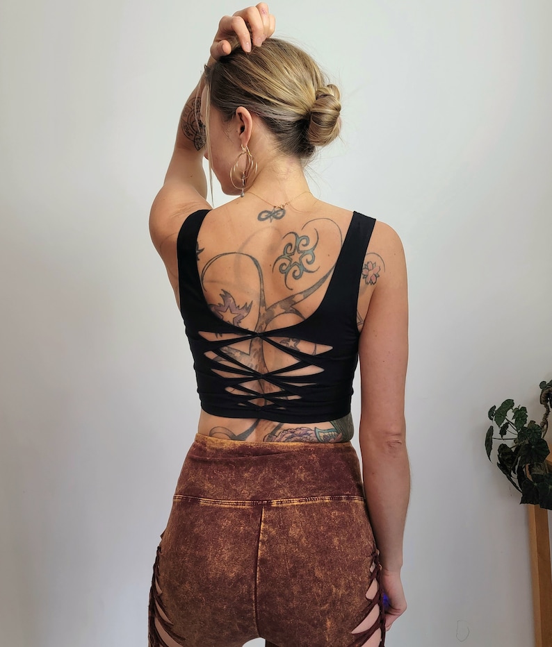 May include: Black crop top with a criss-cross back design. The top is made of a stretchy, comfortable fabric and has a relaxed fit. The model is wearing brown shorts with a distressed look.