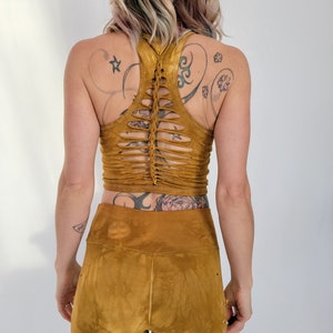 May include: A mustard yellow crop top with a unique criss-cross design on the back. The top is made of a soft, stretchy fabric and has a relaxed fit.