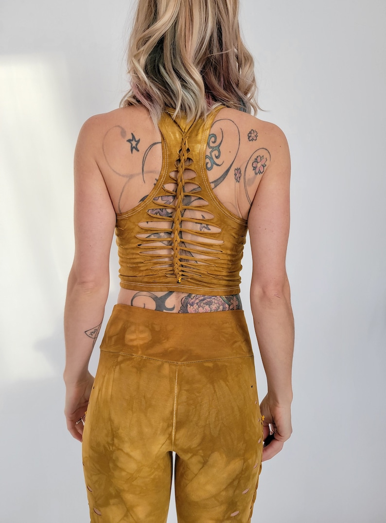 May include: A mustard yellow crop top with a unique criss-cross design on the back. The top is made of a soft, stretchy fabric and has a relaxed fit.