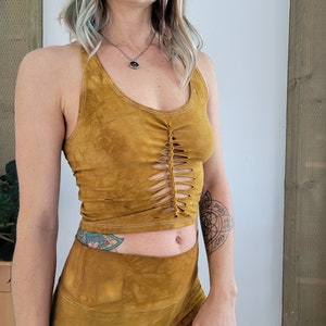 May include: A mustard yellow crop top with a braided detail at the front and matching mustard yellow pants. The top has a scoop neck and the pants have a high waist.