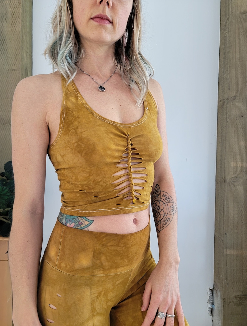 May include: A mustard yellow crop top with a braided detail at the front and matching mustard yellow pants. The top has a scoop neck and the pants have a high waist.