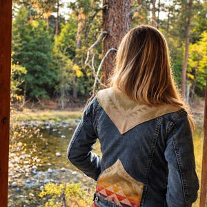Puede incluir: Una chaqueta de mezclilla azul con un panel triangular grande de color tostado en la parte superior de la espalda con un patrón geométrico y un panel triangular más pequeño en la parte inferior con un diseño geométrico multicolor en rojo, naranja y morado.