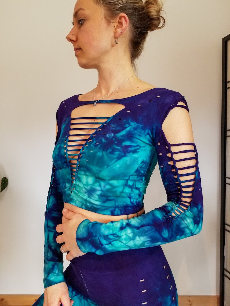 Pu&ograve; includere: Un top corto blu e verde tie-dye con maniche lunghe e tagli alle spalle e al collo. Il top &egrave; realizzato in un tessuto morbido ed elastico.