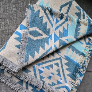 May include: A blue and beige throw blanket with a geometric pattern and fringe trim.