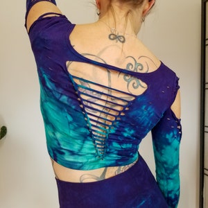 Pu&ograve; includere: Un top corto a maniche lunghe con stampa tie-dye e un design con schiena scoperta. Il top &egrave; una miscela di colori turchese, blu e viola. Le maniche hanno un aspetto consumato con piccoli strappi.