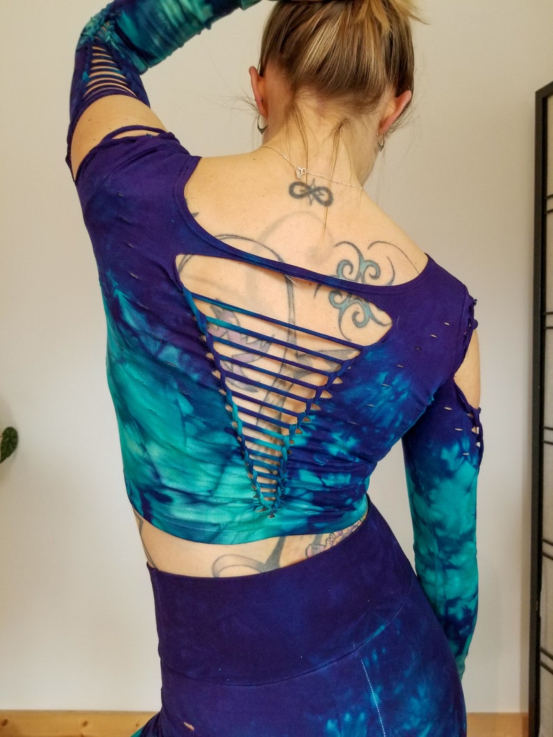 Pu&ograve; includere: Un top corto a maniche lunghe con stampa tie-dye e un design con schiena scoperta. Il top &egrave; una miscela di colori turchese, blu e viola. Le maniche hanno un aspetto consumato con piccoli strappi.