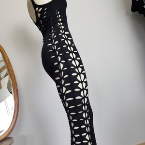 May include: Black maxi dress with a floral cut-out design on the sides. The dress is sleeveless and has a scoop neck.