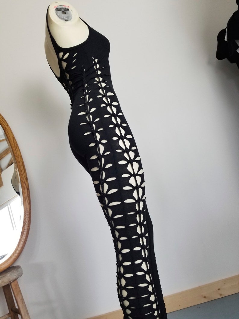 May include: Black maxi dress with a floral cut-out design on the sides. The dress is sleeveless and has a scoop neck.
