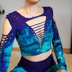 Pu&ograve; includere: Un top corto tie-dye a maniche lunghe con un dettaglio di pizzo sul davanti. Il top &egrave; blu e verde con una sfumatura viola.