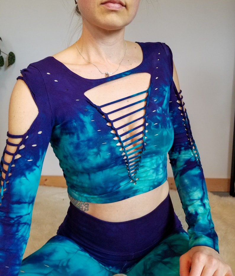 Pu&ograve; includere: Un top corto tie-dye a maniche lunghe con un dettaglio di pizzo sul davanti. Il top &egrave; blu e verde con una sfumatura viola.