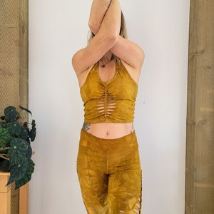 May include: A mustard yellow crop top and matching pants with cutouts. The top has a halter neckline and the pants have a high waist.