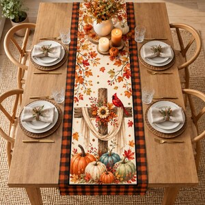 May include: A rectangular table runner featuring a central design of a wooden cross adorned with a sunflower, draped fabric, and a red cardinal, surrounded by autumn leaves and pumpkins, framed by a black and red buffalo plaid border pattern.