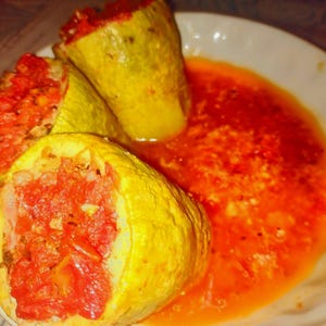 Puede incluir: Tres trozos de calabaza amarilla ahuecados y rellenos con una mezcla roja a base de tomate, dispuestos en un plato blanco junto a una salsa de color naranja rojizo. La piel de la calabaza cocida tiene textura y color amarillo pálido.