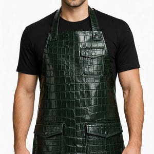 May include: A dark green apron featuring a textured crocodile skin pattern. The apron includes one chest pocket and two lower pockets, each equipped with a flap and a matching dark button closure. The design includes adjustable shoulder straps.