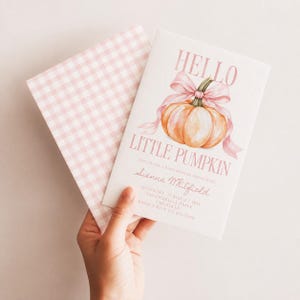 Pode incluir: Um convite de chá de bebé branco com uma abóbora laranja em aguarela com um laço cor-de-rosa, o texto HELLO LITTLE PUMPKIN e detalhes do evento para Sienna Whitfield, acompanhado por um envelope a condizer com padrão xadrez rosa e branco.
