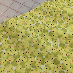 May include: Green fabric with a repeating pattern of small green circles with black eyes and red cheeks. The circles are on a white background.