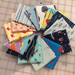 May include: A collection of folded fabric squares with various beach-themed patterns. Designs include crabs, seashells, seahorses, sailboats, and beach umbrellas. The fabrics feature a range of colors, including blue, yellow, red, and white, creating a summery aesthetic.