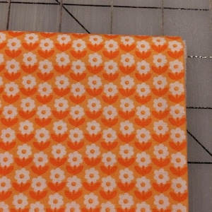 May include: Orange fabric with a white floral pattern. The fabric has a repeating pattern of small white flowers with orange centers.