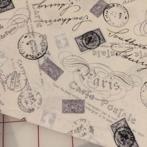 May include: Cream-coloured fabric with a vintage postcard design. The fabric features grey stamps, script, and the words "Carte Postale" and "Paris". The design includes the Eiffel Tower and the word "Amsterdam".