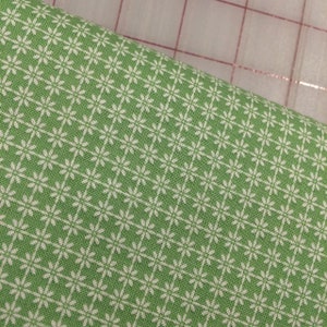 May include: Green fabric with a white floral pattern. The fabric has a subtle texture and a repeating pattern of small white flowers.