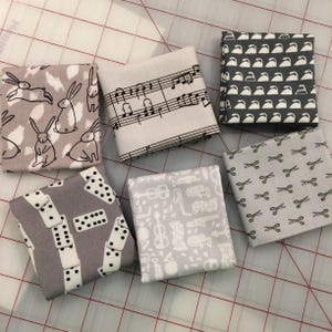 May include: A collection of six fabric squares with various patterns. Designs include rabbits, musical notes, teapots, scissors, dominoes, and musical instruments. The fabrics are in shades of gray, white, and black.