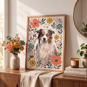 Pode incluir: Uma impress&atilde;o de arte de parede emoldurada apresentando o retrato de um c&atilde;o pastor australiano rodeado por uma ilustra&ccedil;&atilde;o floral colorida de flores laranja, amarelas e azuis e folhas verdes num fundo creme, numa moldura de madeira clara.