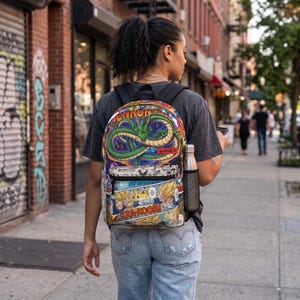 Peut inclure: Un sac à dos avec un imprimé graphique coloré représentant le dragon vert Shenron et des planches de manga Dragon Ball Z. Le design inclut le texte SHENRON et KRA-KOOM. Le sac possède une poignée supérieure noire, des bretelles et une poche latérale en filet.
