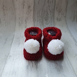 May include: A pair of red knitted baby booties with white pom-poms.