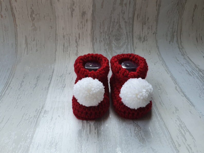 May include: A pair of red knitted baby booties with white pom-poms.