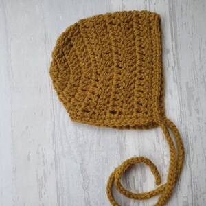 May include: A crocheted baby bonnet in a mustard yellow color with a long tie.