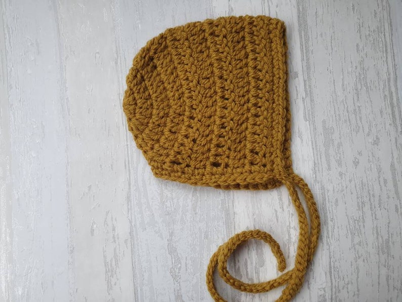 May include: A crocheted baby bonnet in a mustard yellow color with a long tie.