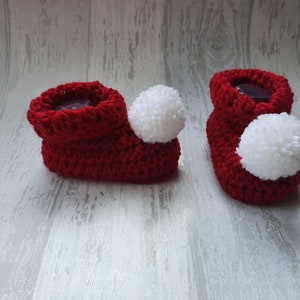 May include: A pair of red crocheted baby booties with white pom-poms.