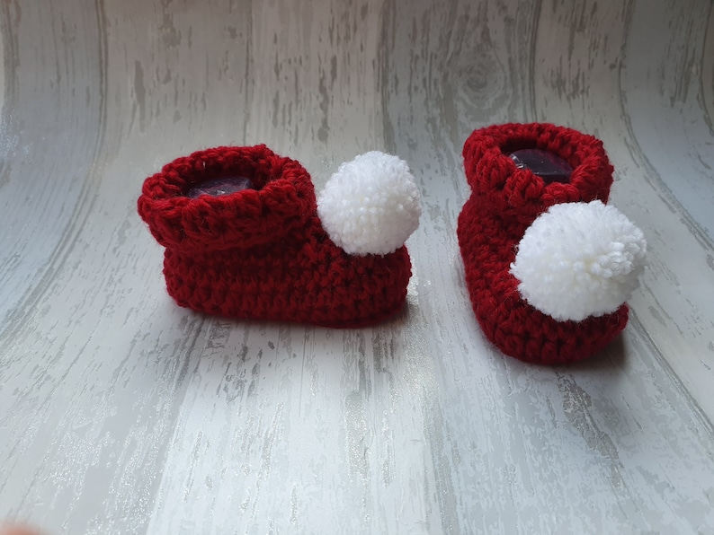 May include: A pair of red crocheted baby booties with white pom-poms.