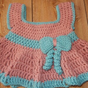K&ouml;nnte beinhalten: Ein geh&auml;keltes Babykleid in Rosa und Blau. Das Kleid hat eine Schleife vorne und einen R&uuml;schenrock.
