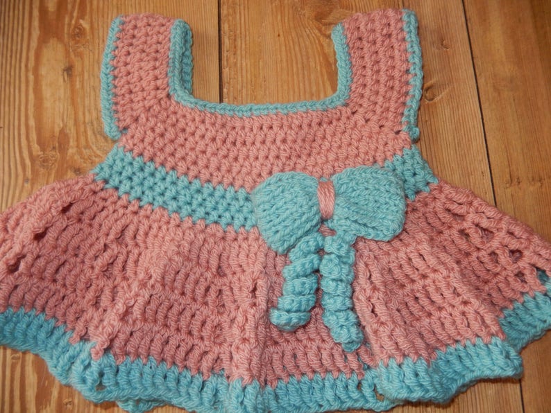 K&ouml;nnte beinhalten: Ein geh&auml;keltes Babykleid in Rosa und Blau. Das Kleid hat eine Schleife vorne und einen R&uuml;schenrock.